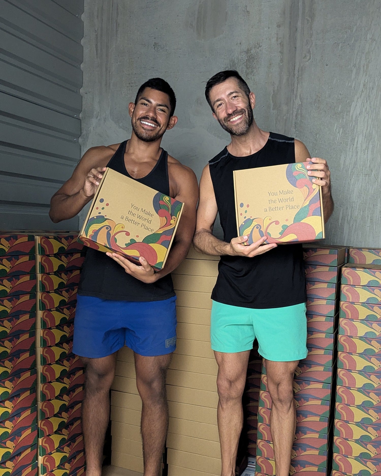 Two men holding boxes in a room with colorful boxes surrounding them.
